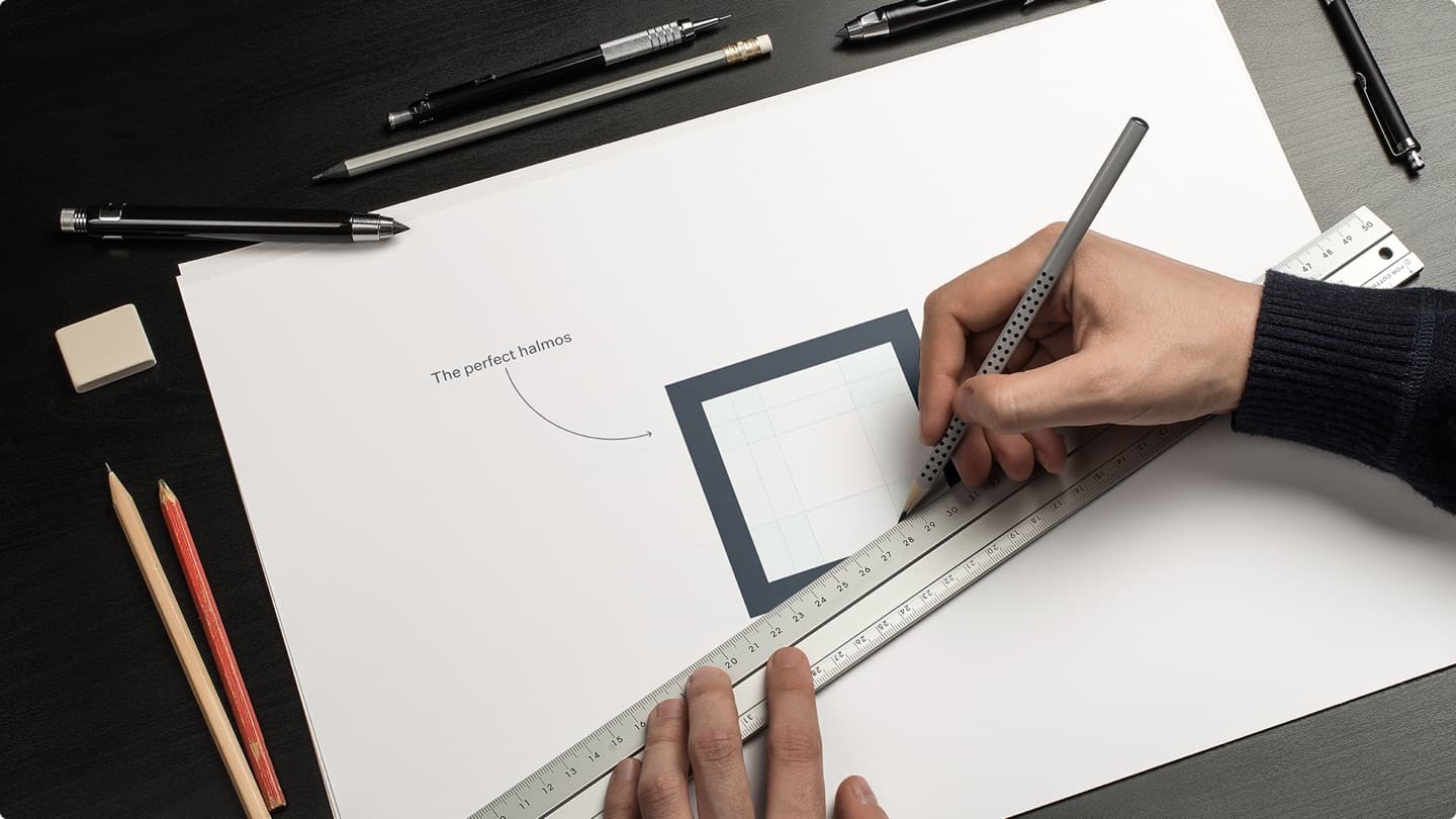 Brand-craft photo — drafting a logo frame by hand with ruler and pencils